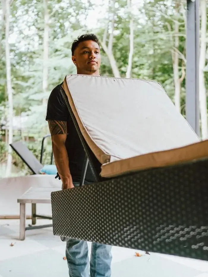A Furniture Disposal Plus Loader carrying a patio lounger and cushion out of a screened porch