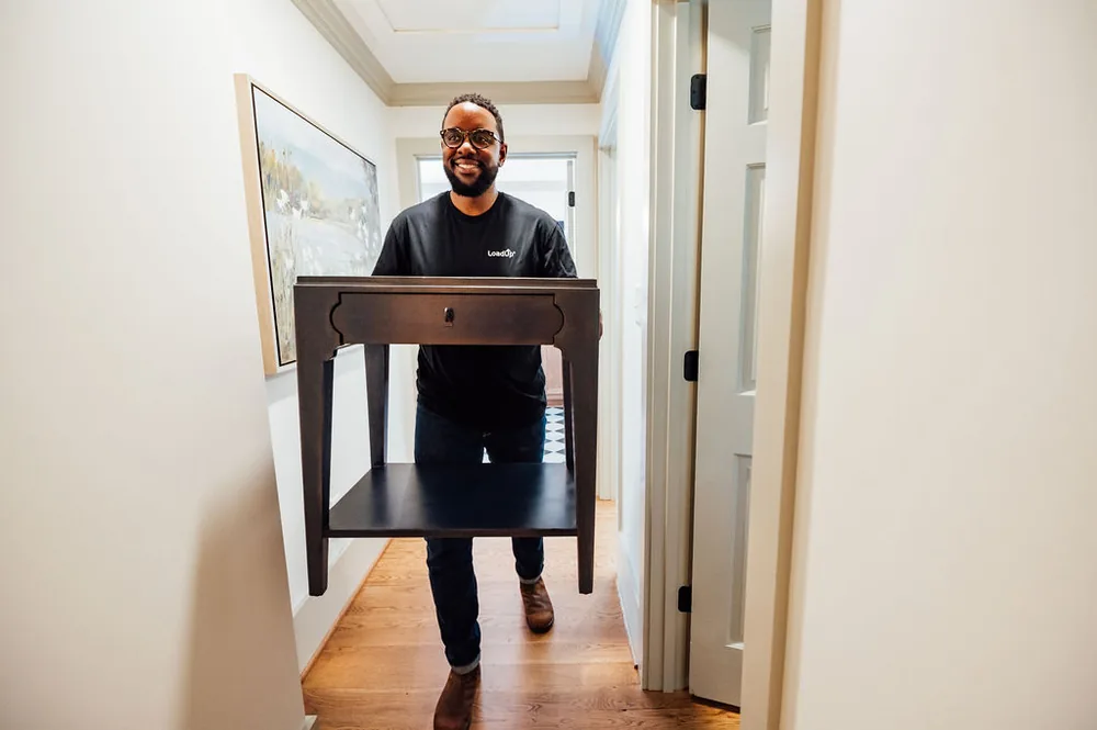 A LoadUp Loader carrying a dark wood nightstand down a residential hallway toward the door