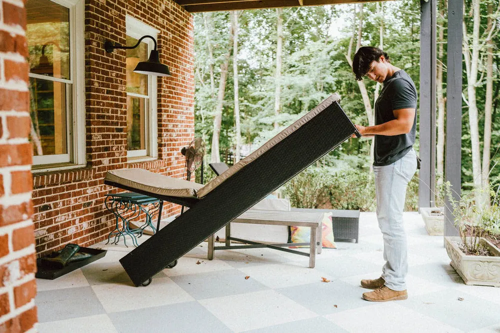 A LoadUp Loader tilting a black wicker patio lounge chair onto a dolly on a brick-lined porch