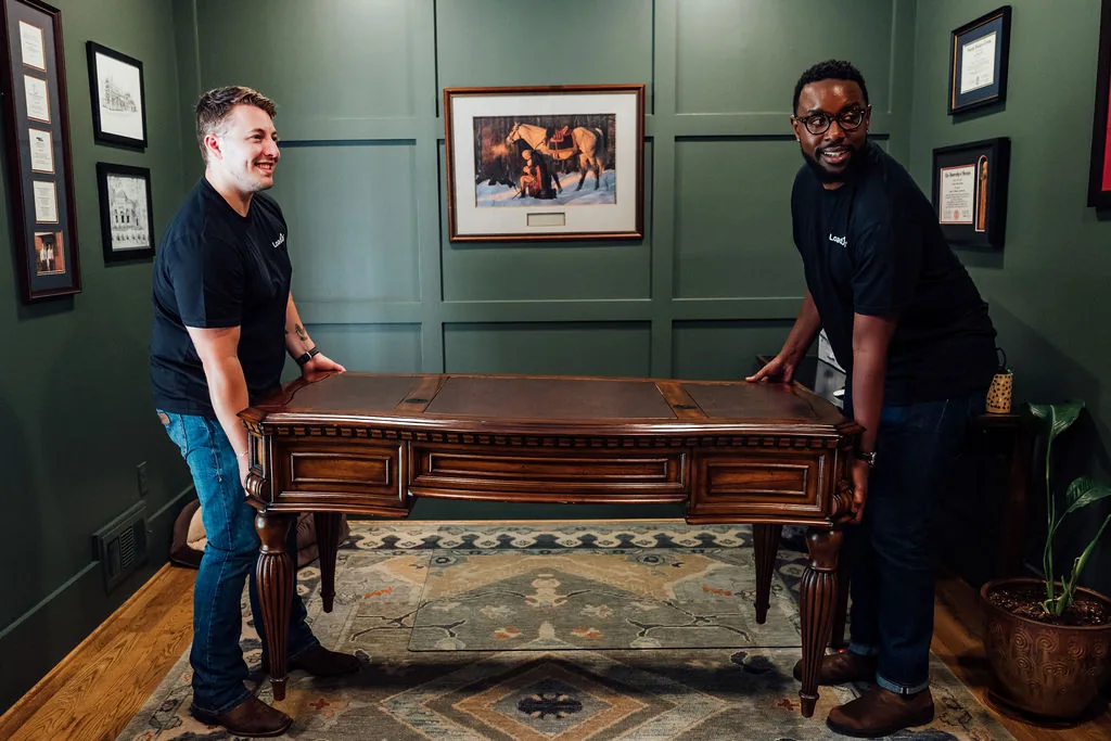 Two LoadUp Loaders carrying a wooden executive desk out of a home office