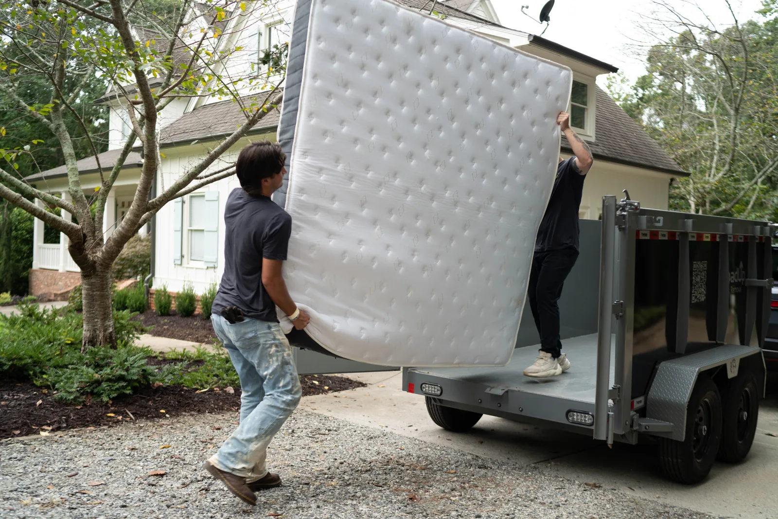 Two LoadUp Loaders lifting a queen mattress onto a LoadUp trailer in a driveway