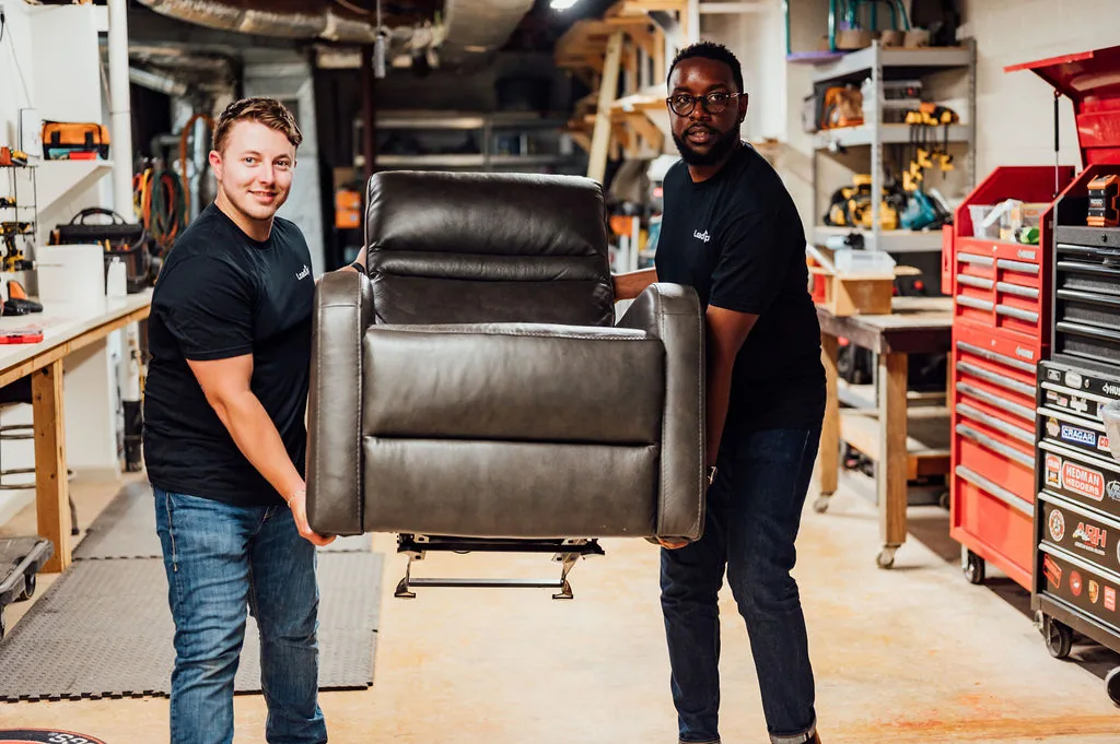 Two LoadUp Loaders carrying a black leather recliner out of a basement workshop