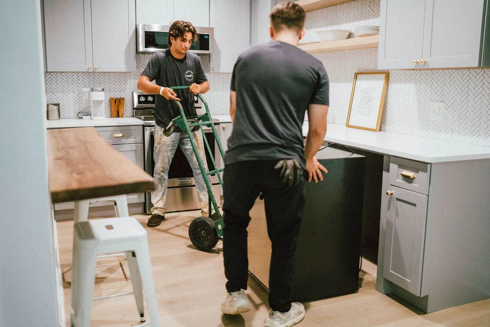 Two Furniture Disposal Plus Loaders pulling a dishwasher out from under a kitchen counter onto a dolly