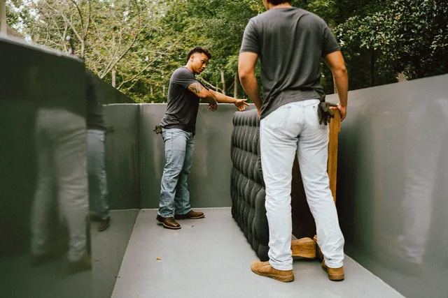 Two Furniture Disposal Plus Loaders lifting a gray sectional into the back of a box truck