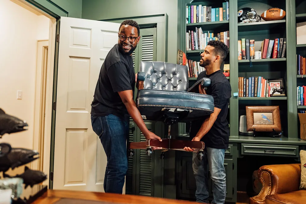 Two LoadUp Loaders lifting a blue leather office chair through a doorway from a book-lined study